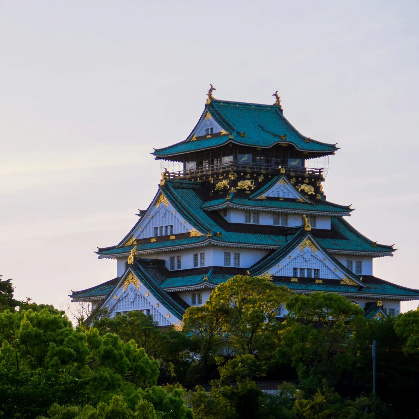 Osaka Castle's green-roofed keep rising above a line of trees at dusk