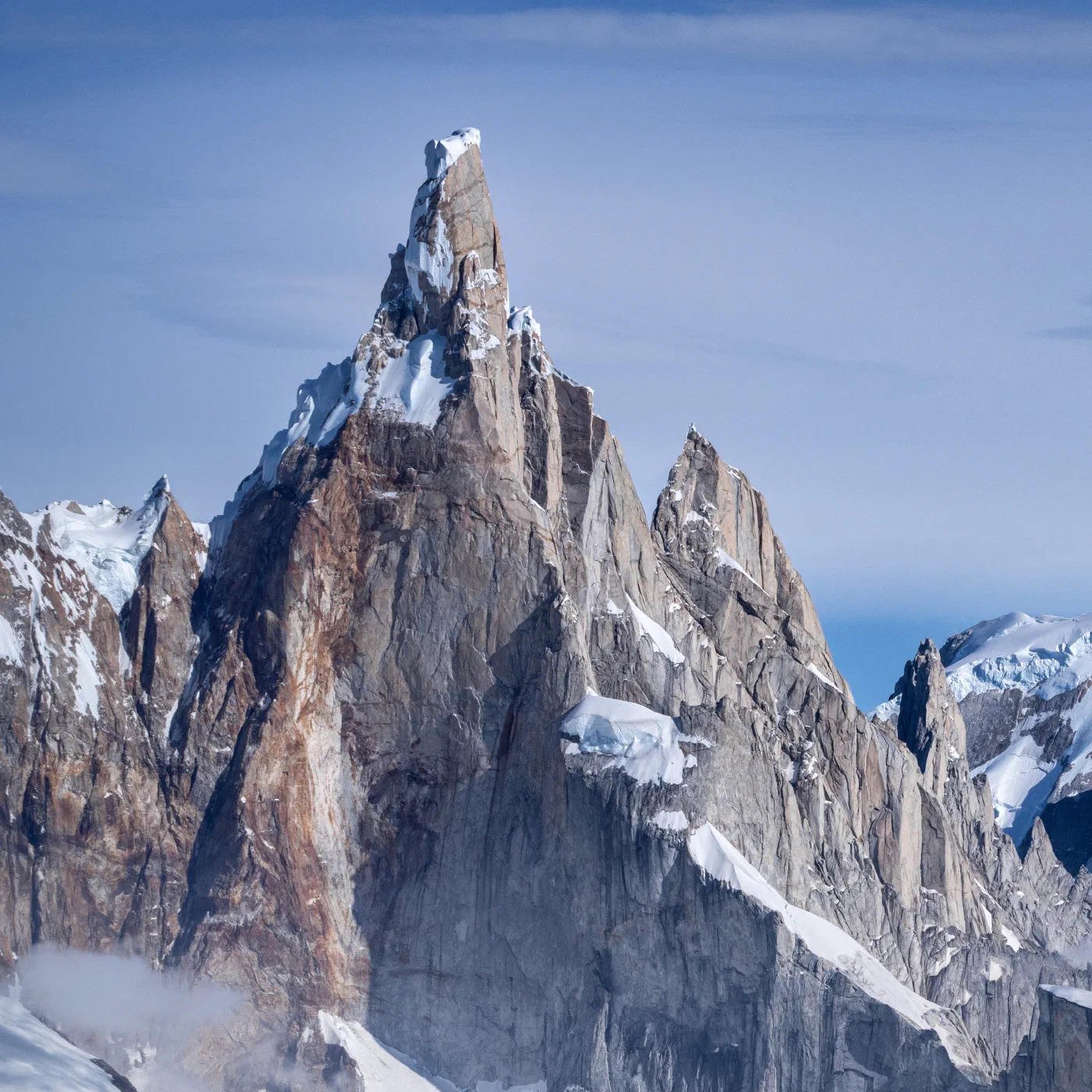 A sharp granite spire rising above snow-covered peaks under a clear sky