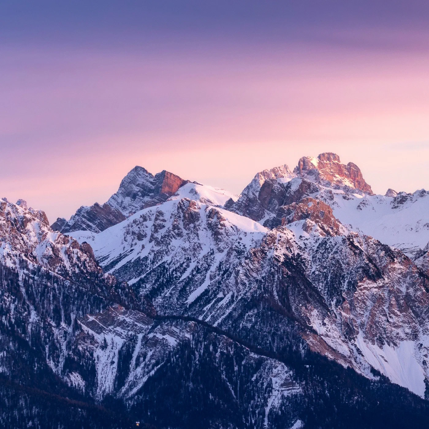 A jagged snow-capped mountain range lit pink and purple at dusk